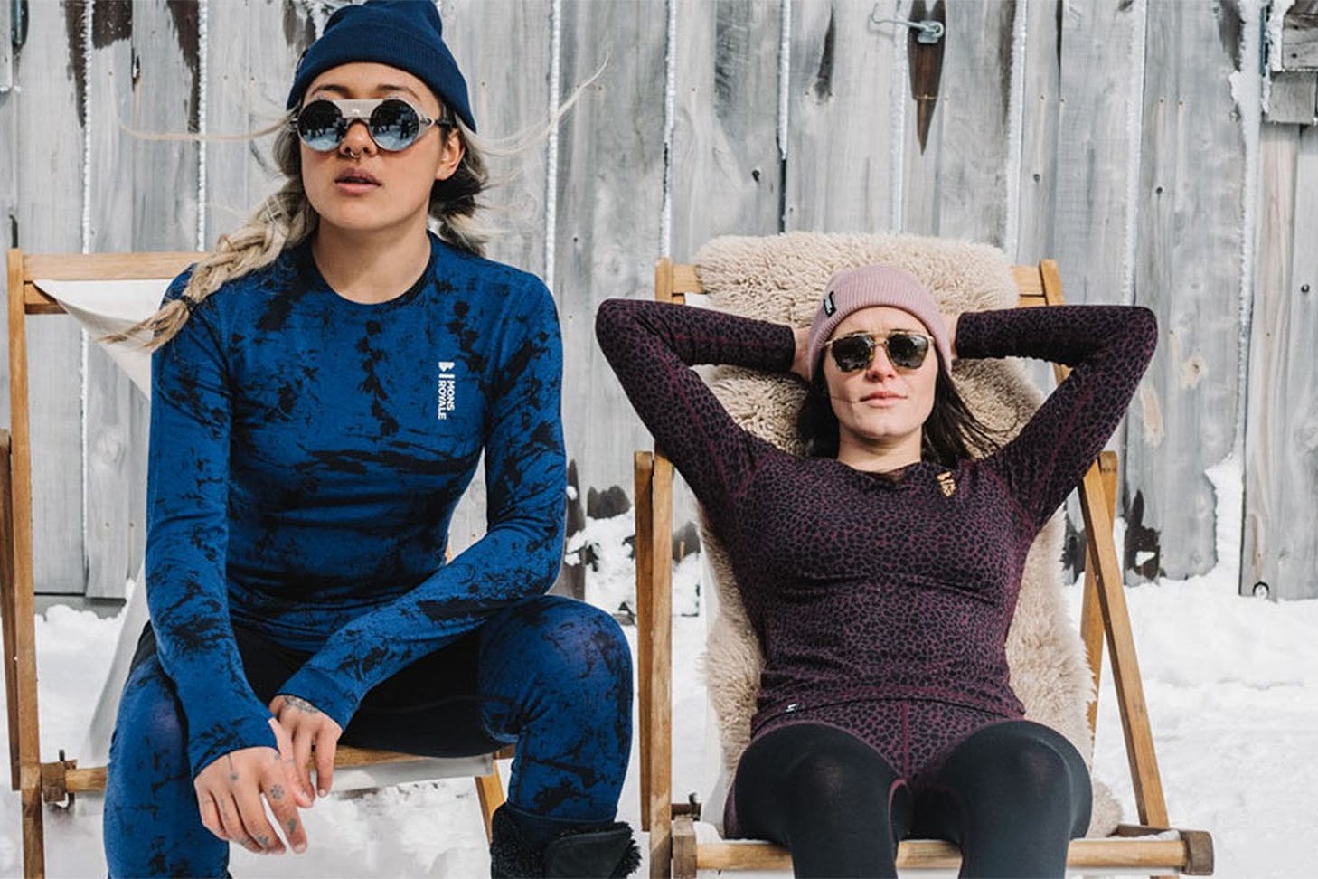 Two people clad in Mons Royale merino baselayers, beanies and sunglasses kick back on chairs in the snow.